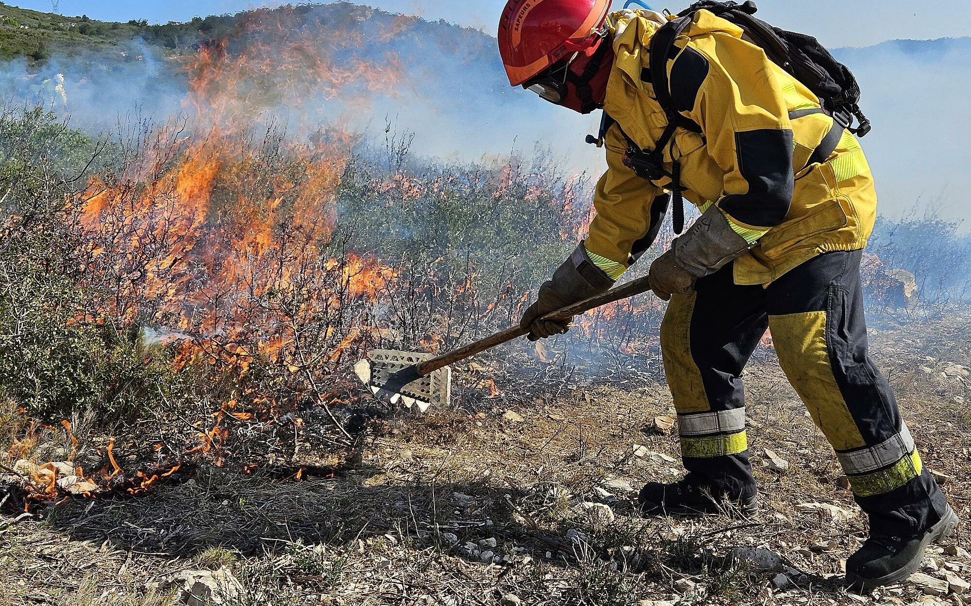 A l'aide d'un râteau, un sapeur a pour mission de gratter la végétation sèche pour empêcher le feu de s'étaler en forêt départementale des Domaines De L'Etoile (13)